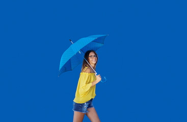 Beautiful smiling Caucasian teenage girl in yellow blouse walking with blue umbrella.
