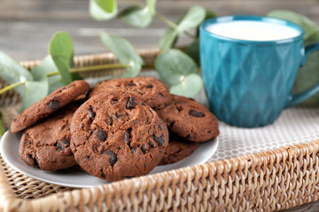 Wicker tray with tasty chocolate cookies and cup of milk, closeup