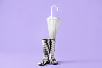 Gumboots and umbrella on color background