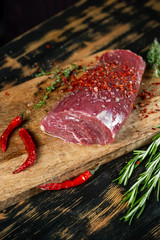 Raw beef fillet steak cooking with herbs, spices, garlic, salt and pepper on wooden table background.
