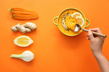 Female hand with spoon, pot of tasty cream soup and ingredients on color background