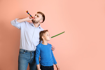 Father and his little son with party whistles on color background