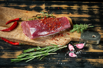 Raw beef fillet steak cooking with herbs, spices, garlic, salt and pepper on wooden table background.