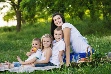 Happy woman with her three kids sits on the plaid outdoor. Family picnic