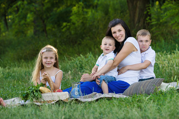 Fototapeta premium Happy woman with her three kids sits on the plaid outdoor. Family picnic