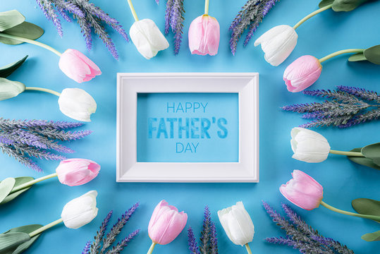 Happy fathers day concept. Top view of white pink tulip flowers and picture frame with Happy father's day text on bright blue pastel background. Flat lay.