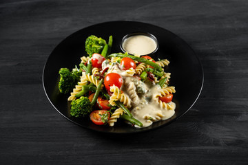 Salad with pasta fusilli, sauce and vegetables in black plate background.