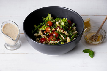 Cold Italian salad with pasta and vegetables in black bowl on white background.