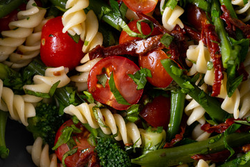 Cold Italian salad with pasta and vegetables in black bowl on white background.