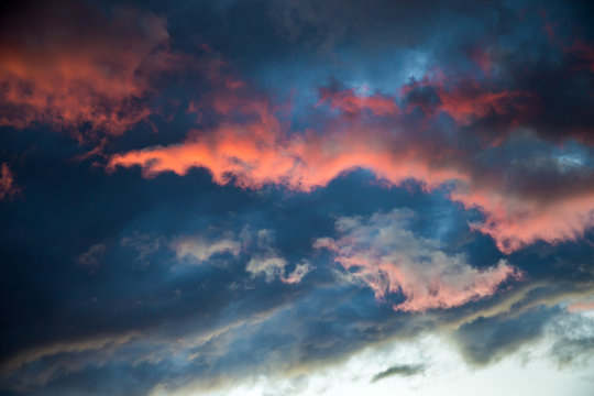 A stormy sky with a bright red glow. Colorful image of dramatic cloudscape. Amazing clouds of pink, white, gray color on the background of the evening dark sky after sunset.