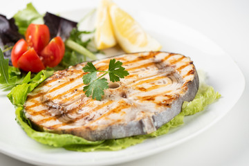 Grilled wordfish with salad and lemon on the white plate