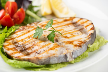 Grilled wordfish with salad and lemon on the white plate