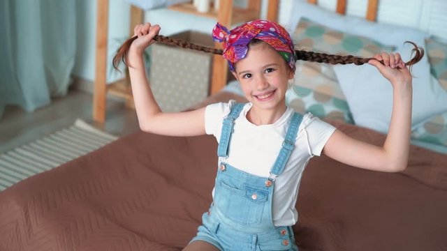 Portrait of smiles girl plays with long braids, grimaces at camera, slow motion
