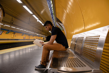 young man reading a book at the subway station