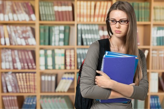 Beautiful female student in library with notebook