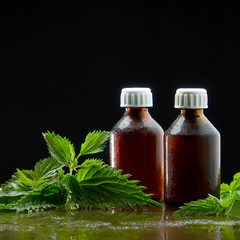 Two jars with a medical infusion of a decoction of nettle with nettle leaves on a black background