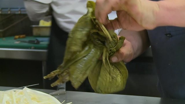 Extreme close-up low-angle still shot of a chef using a knife to unwrapped boiled sea-food from a banana leaf at restaurant kitchen, Callao, Lima, Peru