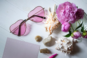 Obraz na płótnie Canvas Pink glasses, peonies and sea shells on a white wooden table. Romantic summer flat lay.