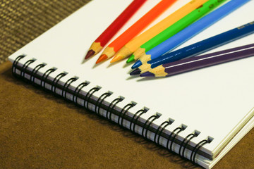 Empty notebook and colorful pencils on brown background