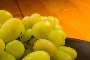large brush of green grapes in a dark ceramic plate on a wooden background