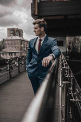 Portrait of handsome fashion businessman model dressed in elegant suit posing on street background. City urban style. Success lifestyle