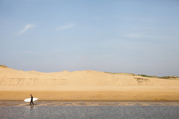 A lonely surfer going in a sunset light. evening in the ocean. Blue sky over huge sand dunes. French coast