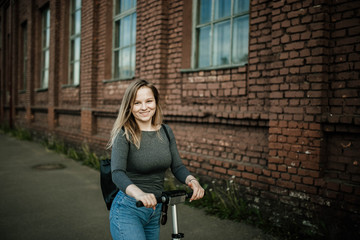 Fototapeta na wymiar young woman driver riding an electric scooter rides the city along a brick wall. The concept of environmentally friendly transport.