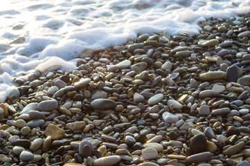 pebble stones on the sea beach, the rolling waves of the sea with foam