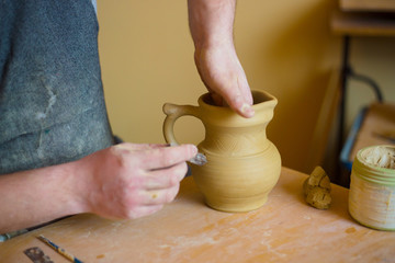 Professional potter making pattern on clay jar with special tool in pottery
