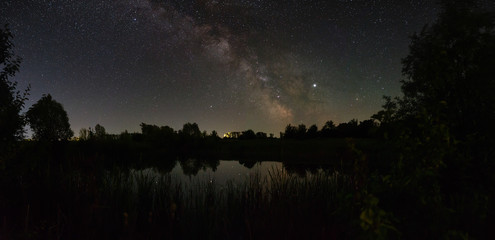 Fototapeta premium Stars in the sky at night. Panoramic view of the bright Milky Way over the lake. Photographed with a long exposure.