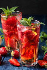 Strawberry Mojito. Cold summer mojito cocktail with strawberries, mint, lemon and ice in a glass on a blue wooden table. on a dark background