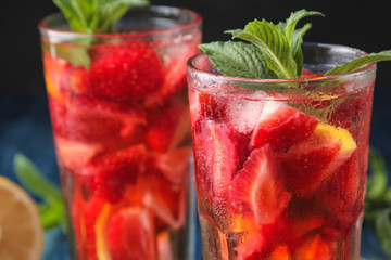 Strawberry Mojito. Cold summer mojito cocktail with strawberries, mint, lemon and ice in a glass on a blue wooden table. on a dark background