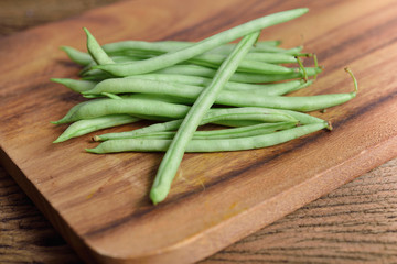 stack of fresh needle beans on wooden cutting board
