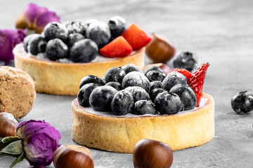 Blueberry and strawberry shortcake. There are hazelnuts, roses and wine corks on the table. Stone background.