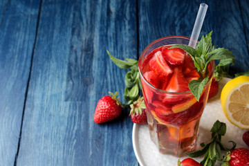 Strawberry Mojito. Cold summer mojito cocktail with strawberries, mint, lemon and ice in a glass on a blue wooden table. on a dark background