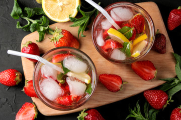 Strawberry Mojito. Cold summer mojito cocktail with strawberries, mint, lemon and ice in a glass on a black table. summer refreshing drink. top view