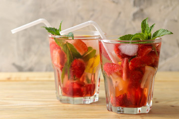 Strawberry Mojito. Cold summer mojito cocktail with strawberries, mint, lemon and ice in a glass on a natural wooden table. summer refreshing drink.