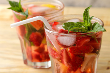 Strawberry Mojito. Cold summer mojito cocktail with strawberries, mint, lemon and ice in a glass on a natural wooden table. A refreshing summer drink. close-up