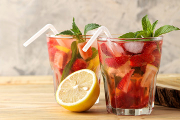 Strawberry Mojito. Cold summer mojito cocktail with strawberries, mint, lemon and ice in a glass on a natural wooden table. summer refreshing drink.