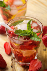 Strawberry Mojito. Cold summer mojito cocktail with strawberries, mint, lemon and ice in a glass on a natural wooden table. A refreshing summer drink. close-up