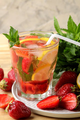 Strawberry Mojito. Cold summer mojito cocktail with strawberries, mint, lemon and ice in a glass on a natural wooden table. summer refreshing drink.