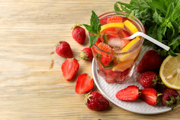 Strawberry Mojito. Cold summer mojito cocktail with strawberries, mint, lemon and ice in a glass on a natural wooden table. summer refreshing drink.
