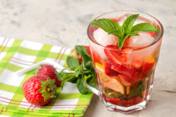 Strawberry Mojito. Cold summer mojito cocktail with strawberries, mint, lemon and ice in a glass on a bright table. summer refreshing drink.