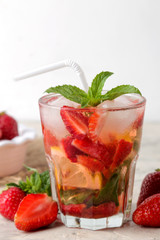 Strawberry Mojito. Cold summer mojito cocktail with strawberries, mint, lemon and ice in a glass on a bright table. summer refreshing drink.