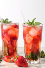 Strawberry Mojito. Cold summer mojito cocktail with strawberries, mint, lemon and ice in a glass on a bright table. summer refreshing drink.
