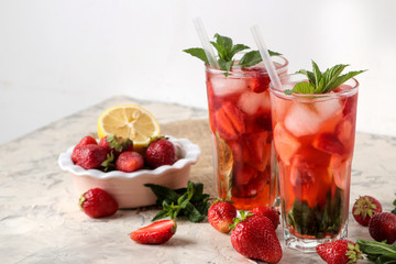Strawberry Mojito. Cold summer mojito cocktail with strawberries, mint, lemon and ice in a glass on a bright table. summer refreshing drink.