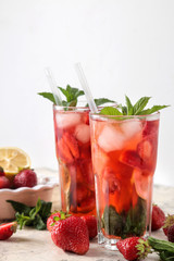 Strawberry Mojito. Cold summer mojito cocktail with strawberries, mint, lemon and ice in a glass on a bright table. summer refreshing drink.