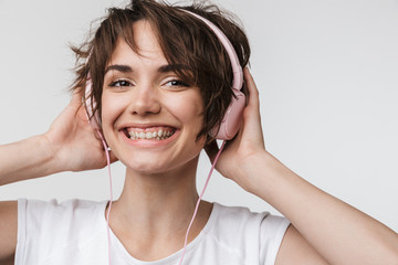 Pretty excited happy woman posing isolated over white wall background listening music with headphones.