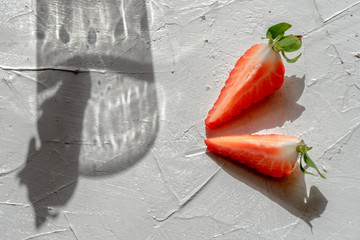 Shadow play from the glass and strawberrie on a white background.Arrangement with strawberry pieces and a glass shadow on a white table