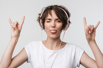 Pretty excited happy woman posing isolated over white wall background listening music with headphones.